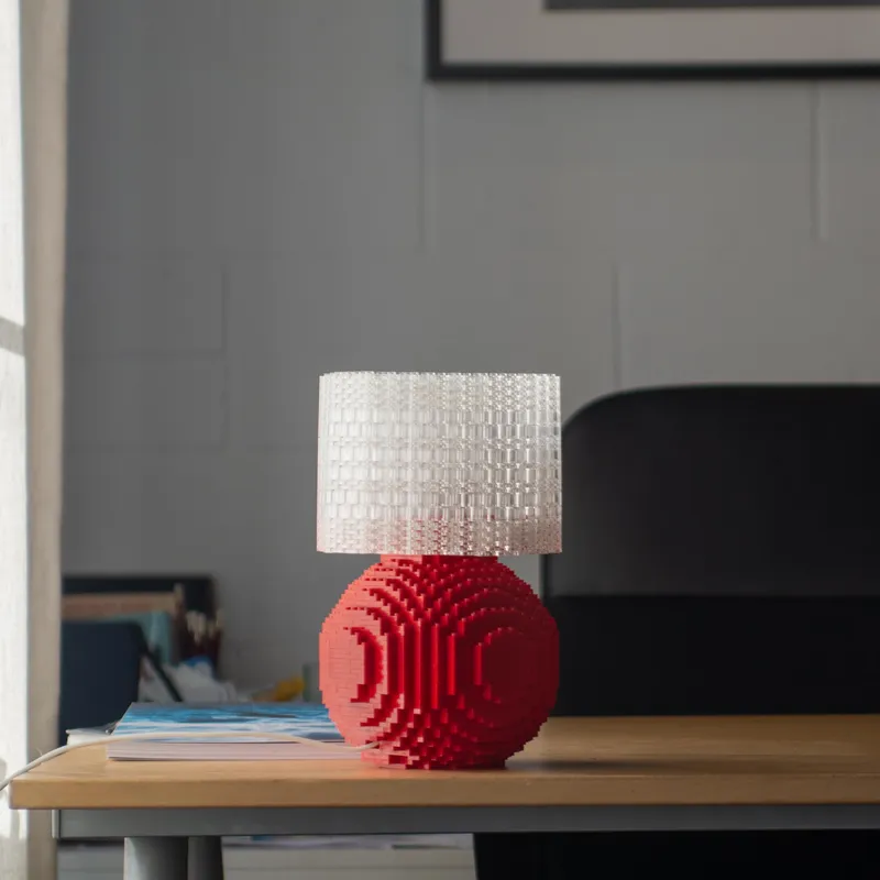A red Splash of Color lamp lit on a wooden desk in a bright modern office.