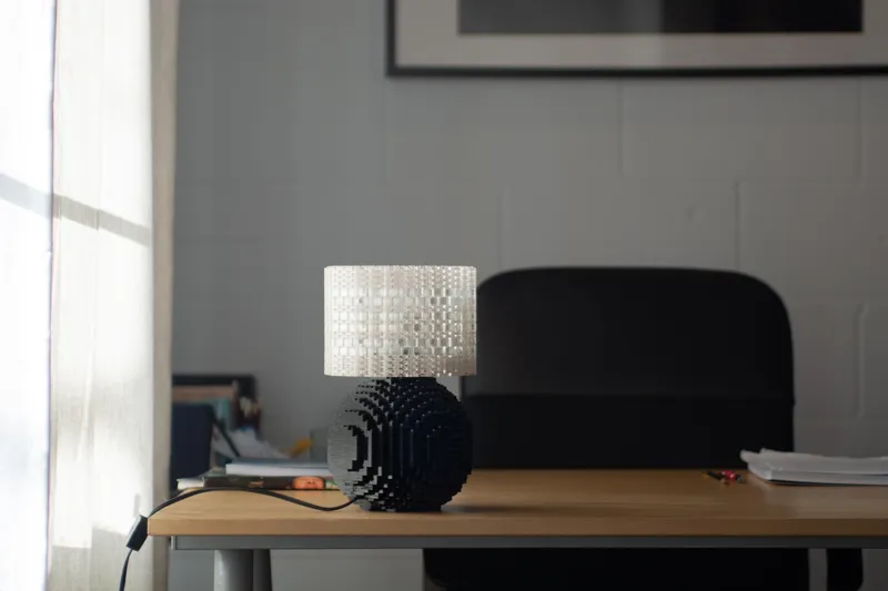 A black-based Splash of Color lamp lit on a wooden desk in a bright modern office.